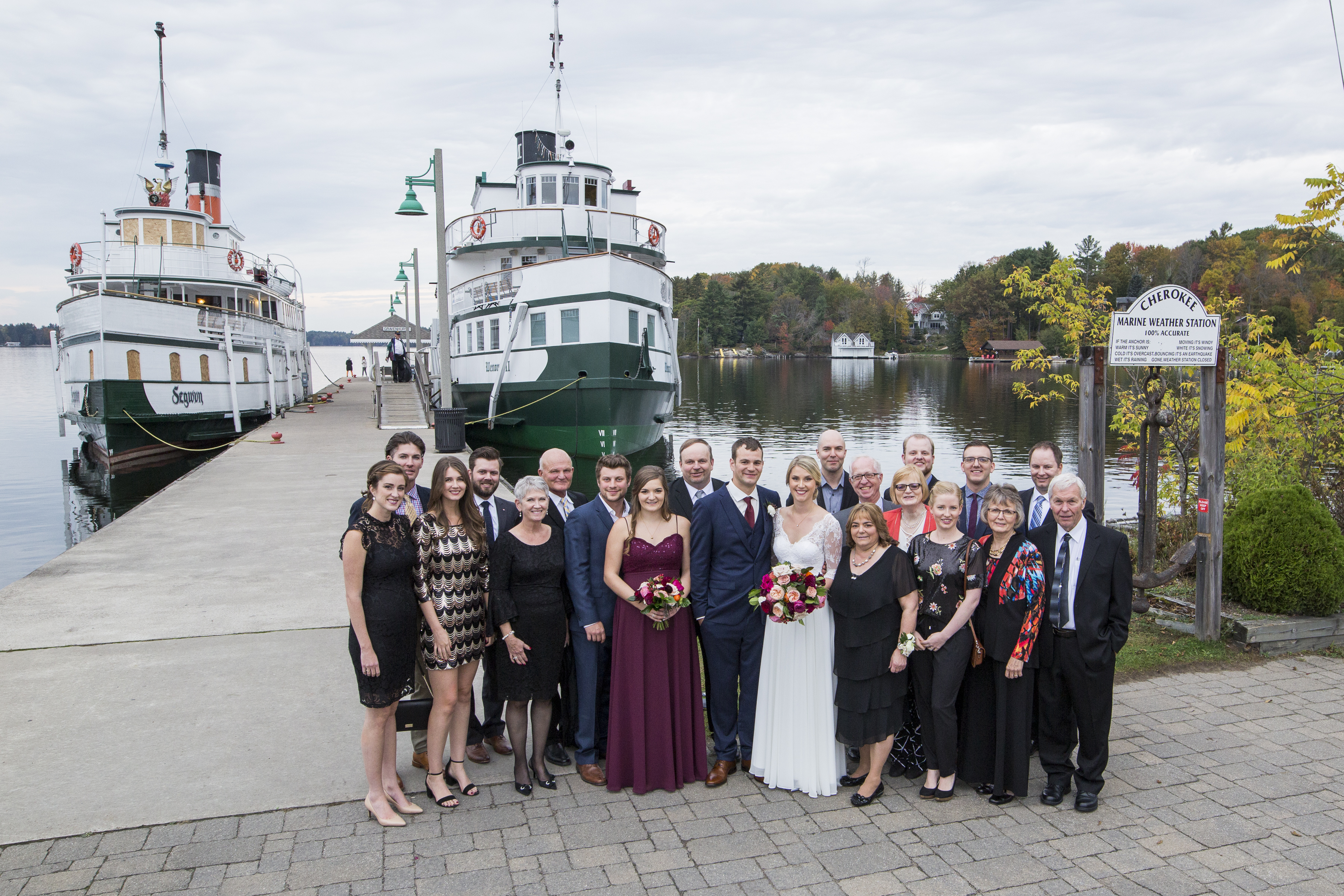 Photo of a wedding party standing at the Muskoka Wharf with the Steamships in the background